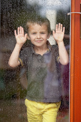 Little boy behind the window in the rain