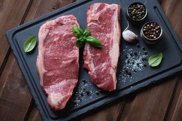 Two raw striploin steaks with sea salt, pepper, garlic and basil