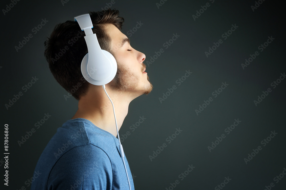 Handsome young man listening to music on grey background
