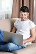 © Africa Studio - Handsome young man sitting on sofa and using laptop in room