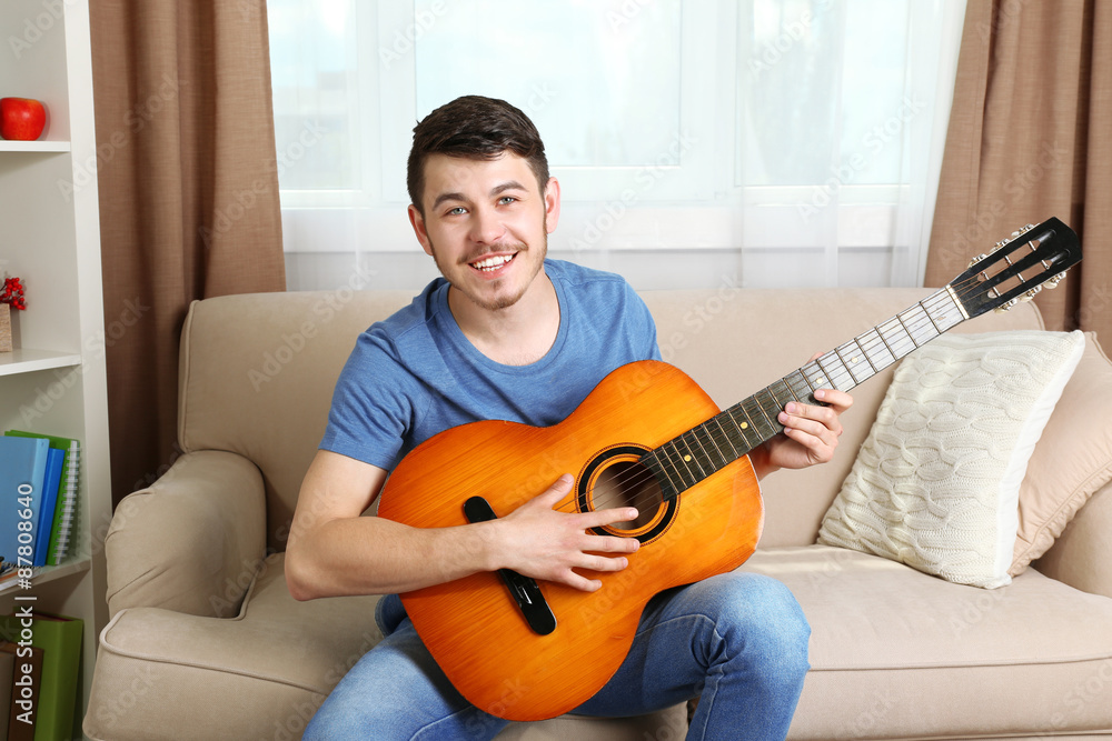 Young man with guitar on sofa in room