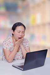 Asian woman yawning in front of notebook computer between workin