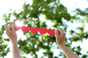 Sticker - Female hands with chain of paper hearts over nature background