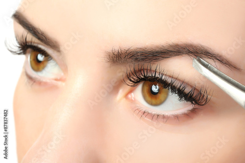 Fotografering Young woman plucking eyebrows with tweezers close up