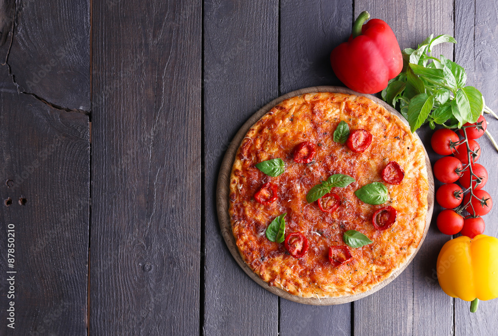 Pizza with basil and cherry tomatoes on cutting board on wooden background