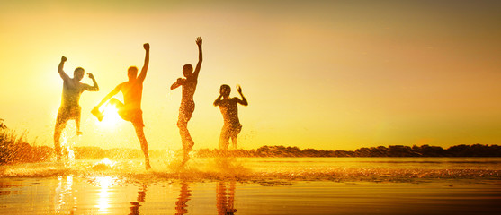 Glückliche junge Menschen laufen und springen am See beim Sonnenuntergang