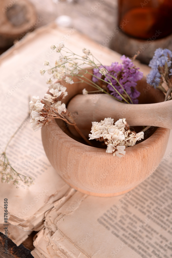 Old book with dry flowers in mortar and bottles on table close up