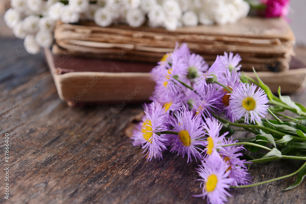 Old books with beautiful flowers on wooden table close up