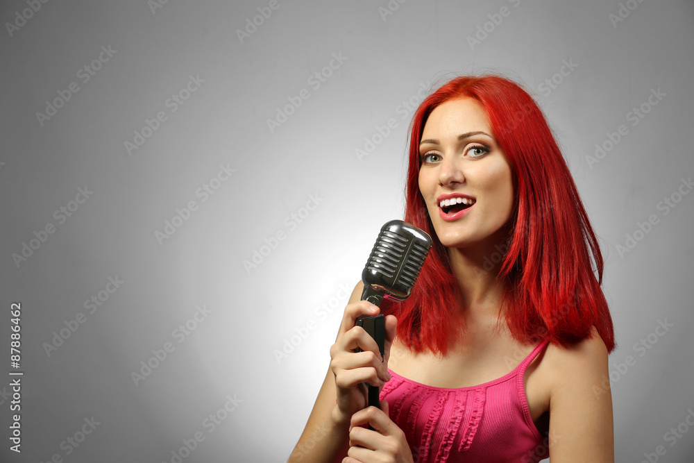 Beautiful young woman with microphone on gray background