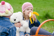 Girl on picnic eats a banana and holds bear