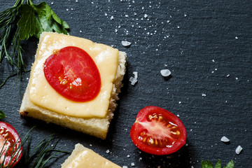 Hot sandwiches with cheese and tomato, greens, on a dark stone b