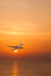 Commercial airplane flying above the sea at sunset