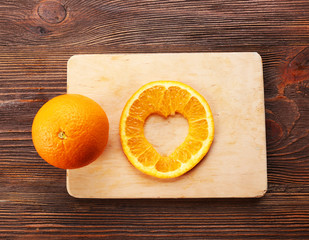 Orange slice with cut in shape of heart and fruit on wooden background