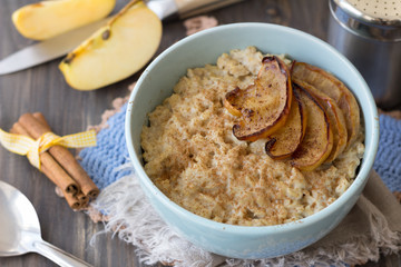 Oatmeal with baked apples and cinnamon in blue ceramic bowl on wooden table