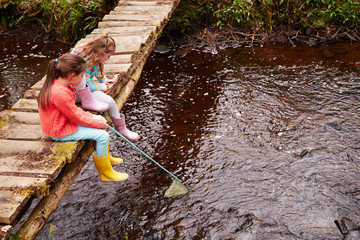 Wall Mural - Two Girls Sitting On Bridge Fishing In Stream With Net