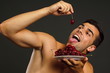 © petrdlouhy - Young man eats red fresh cherry on gray background