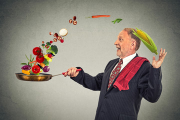 mature happy businessman cooking vegetables with a pan