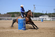 Young blonde woman barrel racing; A young woman turns around a barrel before racing to the finish line