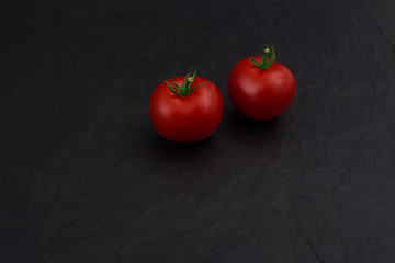 two cherry tomatoes on black slate stone background 