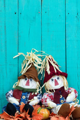 Scarecrows sitting in leaves by rustic fence