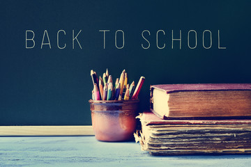 pencils, old books and the text back to school on a chalkboard,