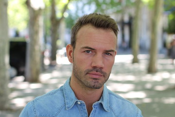 Horizontal close-up portrait of a serious confident young male model with a city stylish background 