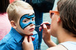 Woman painting face of kid outdoors