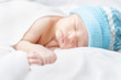Sleeping New born baby boy wearing blue hat covering silk white bed sheet