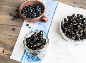 Fresh black mulberries in a glass jar on the gray wooden backgro