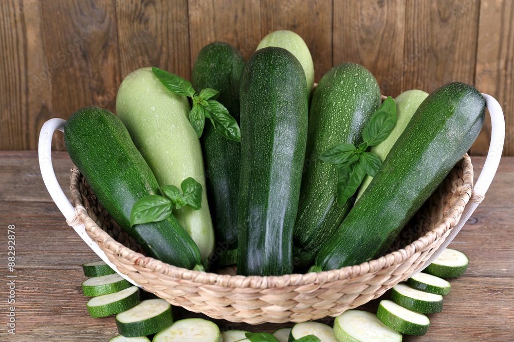 Fresh zucchini with squash and basil in wicker basket on wooden background