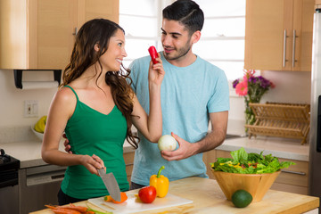 Lovers couple cooking vegetables and preparing an organic salad in the kitchen playful fun funny