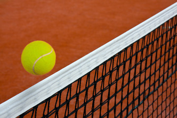 Tennis ball gliding over the net on clay court