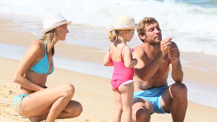 Wall Mural - Parents with little girl playing on a sandy beach