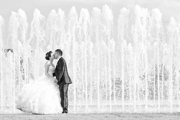 Bride and groom kissing in front of water fountain black and whi