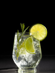 Wall Mural - Gin and tonic cocktail with lime over black background.