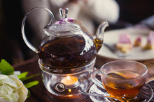 Beautiful Warm Picture Of Transparent Teapot Kettle With Tasty Green Black Tea With Apple, Lemon And Ginger On A Table With Candles And With Dessert In The Background