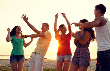 smiling friends dancing on summer beach