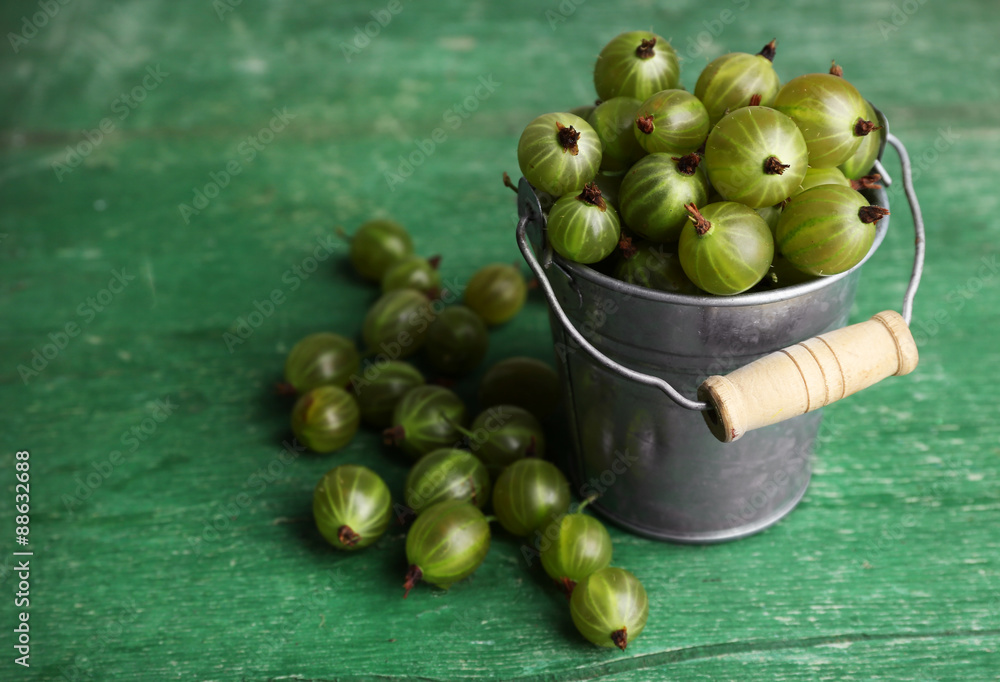Green gooseberry in pail on wooden background