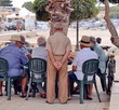 gruppo di anziani che giocano a carte seduti ad un tavolo all'aperto sotto un albero