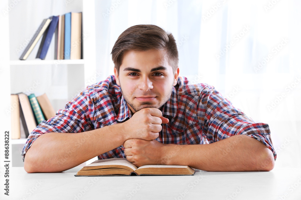 Young man reading book at table in room