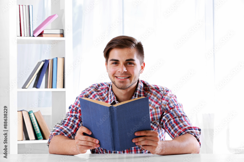Young man reading book at table in room