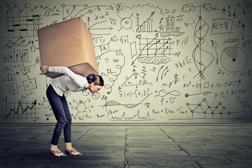 woman carrying heavy box walking along gray wall