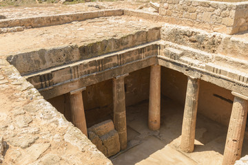 Looking down into the grand chamber of an ancient carved stone burial tomb at an archaeological site in Paphos, Cyprus.