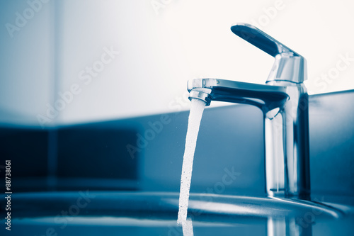 Fotografia  faucet with flowing water, blue tone