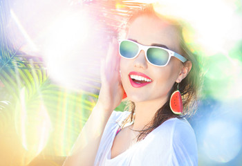 Wall Mural - Colorful summer portrait of happy young attractive woman wearing sunglasses and watermelon earrings, beauty and fashion concept