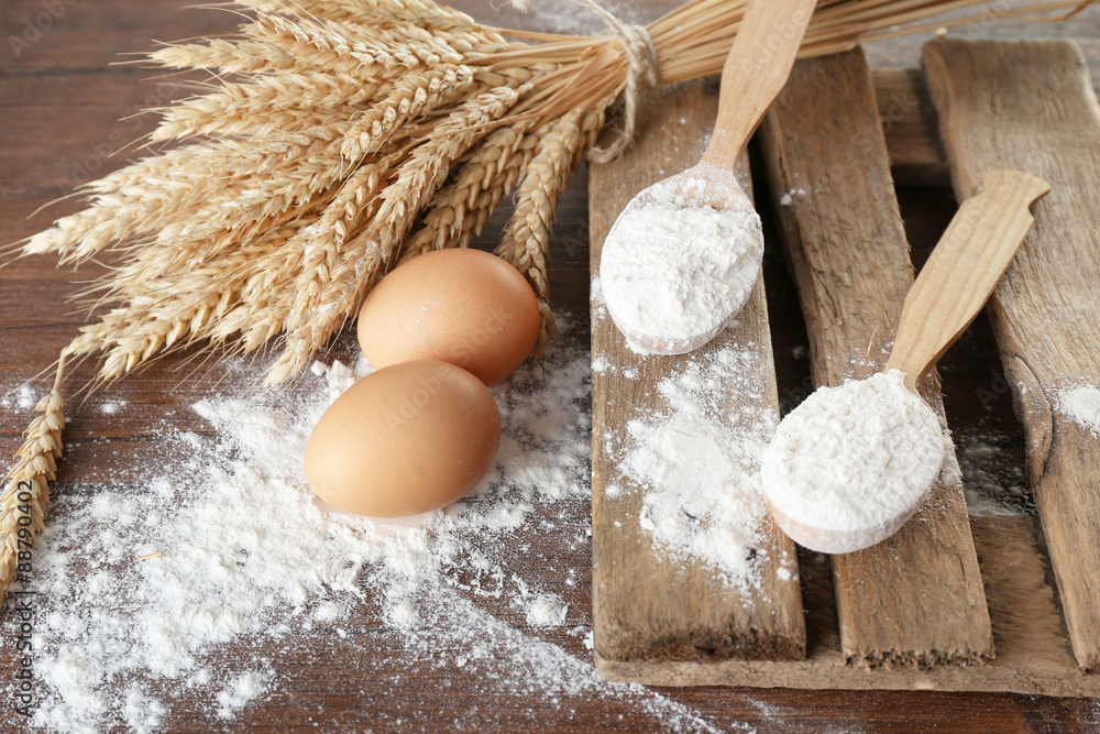 Whole flour with wheat and eggs on wooden table, closeup