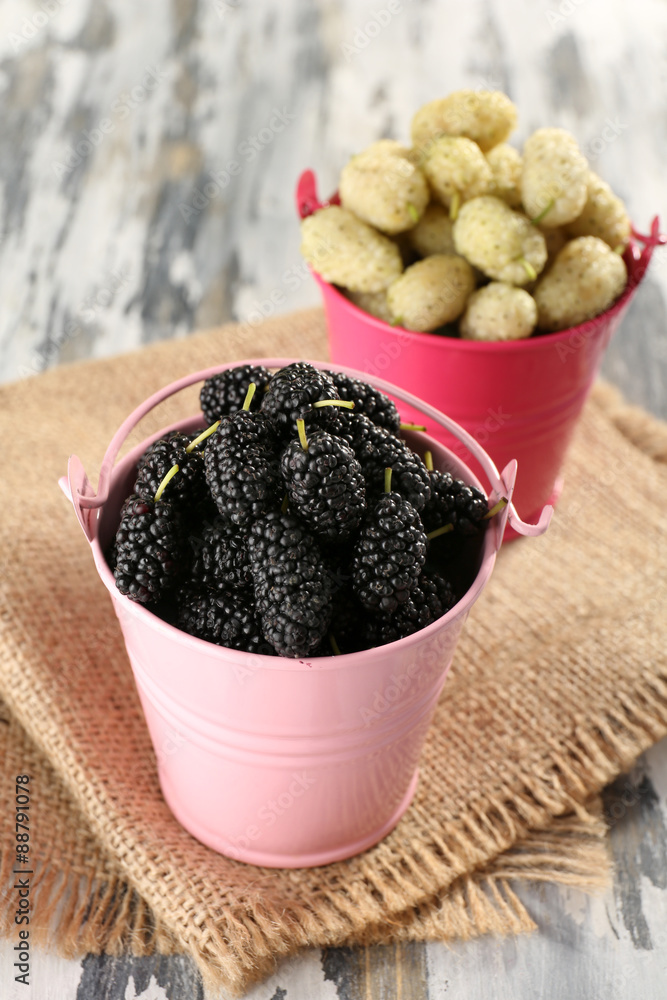 Ripe mulberries in buckets on table close up
