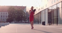 Attractive Business Woman Using Digital Tablet Walking In The City. Slow Motion, 4K. Sexy Woman Wearing Red Dress And High Heel Shoes Enjoying Morning, Drinking Coffee, Reading News. Lens Flare.