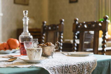 Vintage 1940s interior English table setting with teacup, nuts, wine, and oranges on a lace tablecloth.