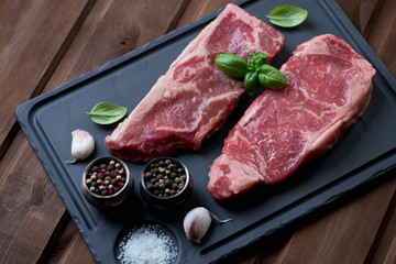 Wall Mural - Two raw black angus steaks striploin on a basalt plate, close-up